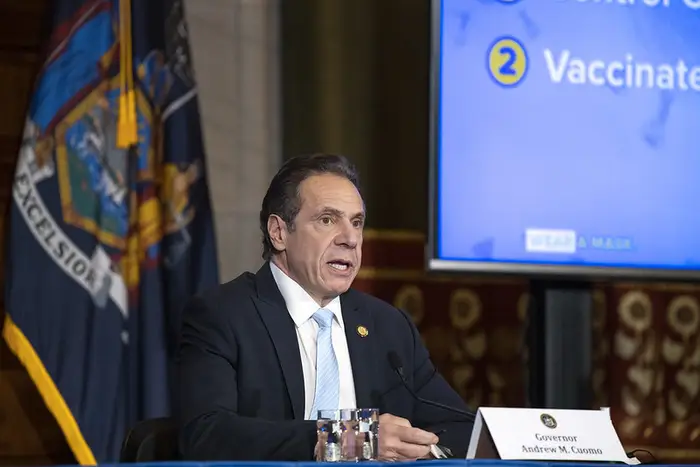 Andrew Cuomo sits at a table wearing a suit during a press conference.